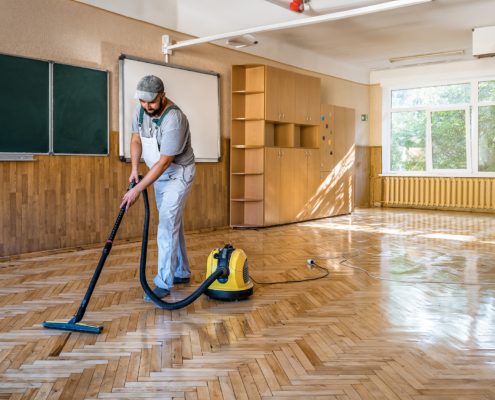 Side view of a man cleaning the floors of an empty classroom