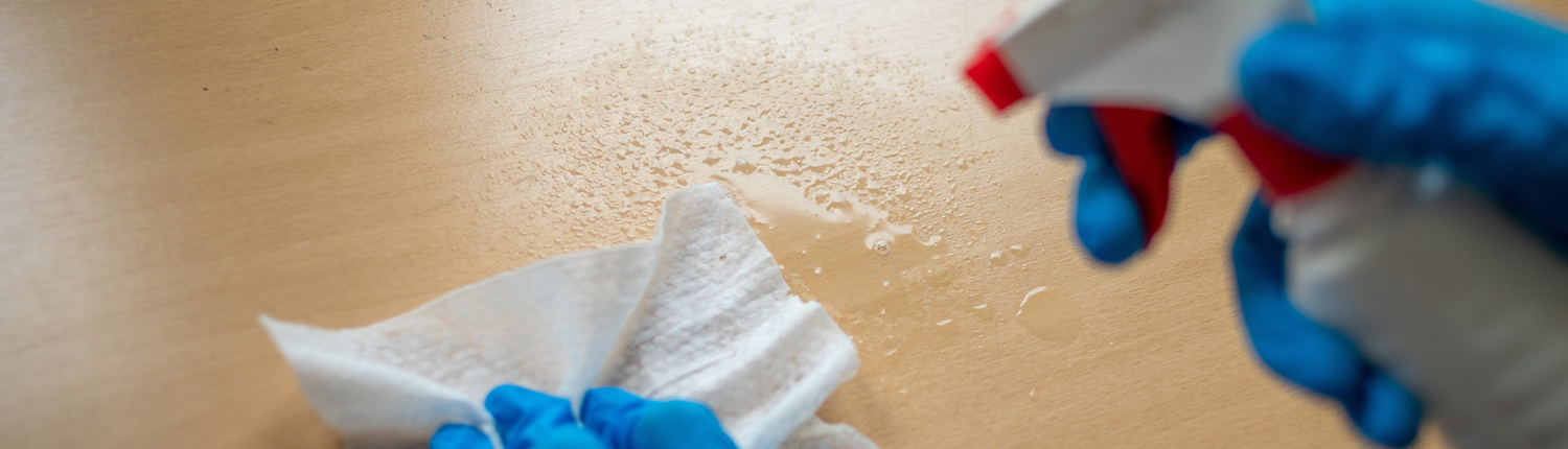 First person view of a wooden surface being wiped down, gloves and towel in view