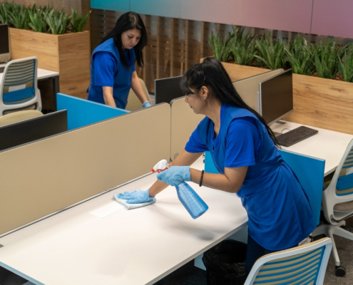 Side view of two professional cleaners wiping down surfaces in office space