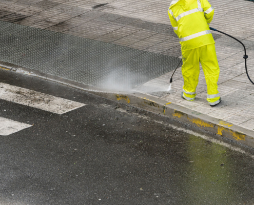 Worker cleaning the sidewalk with pressurized water. Maintenance or cleaning concept